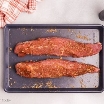 Two pork tenderloins with a spice rub spread on them on a sheet pan.