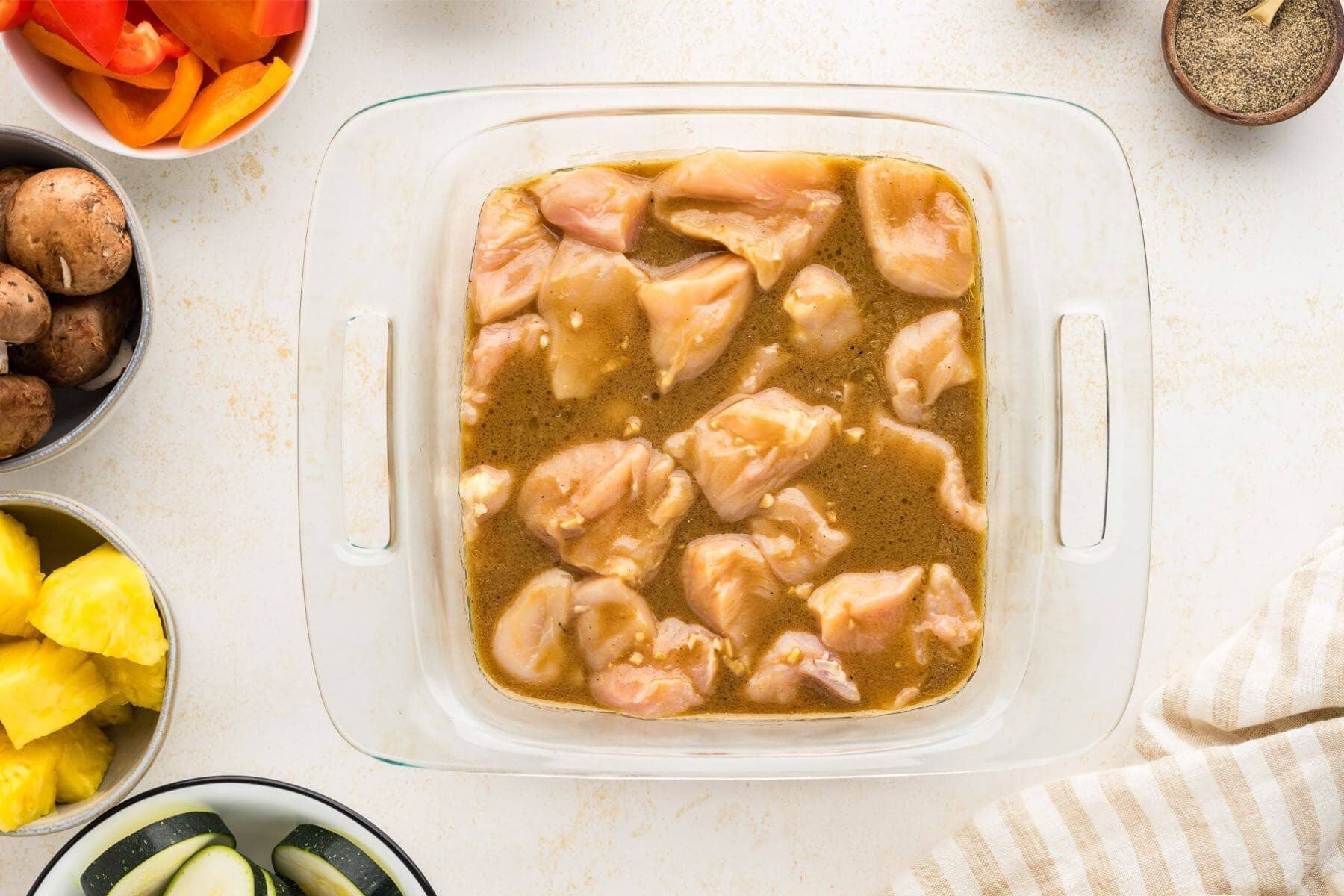 Chicken chunks marinating in shish kabob marinade in shallow dish.