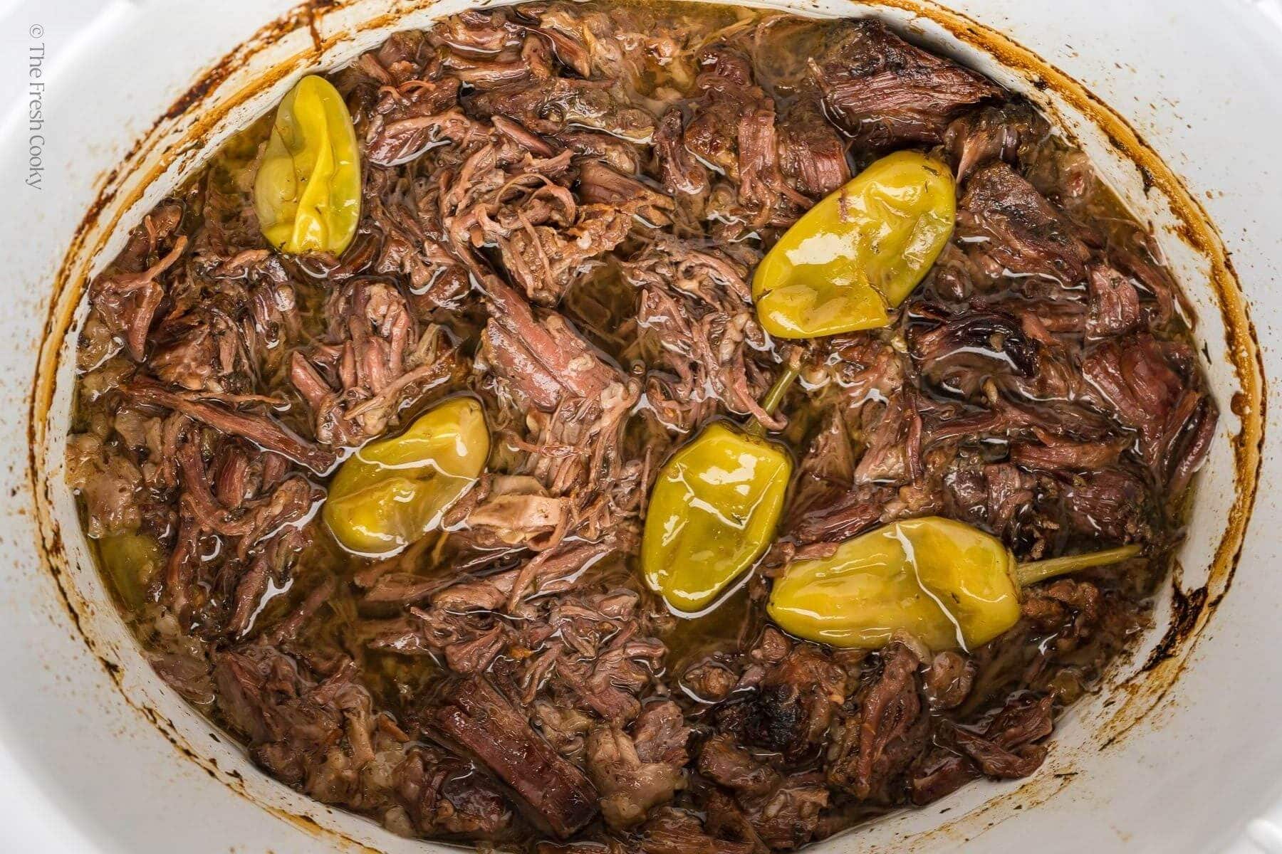 Shredded Mississippi pot roast in a crock pot with pepperoncini peppers.
