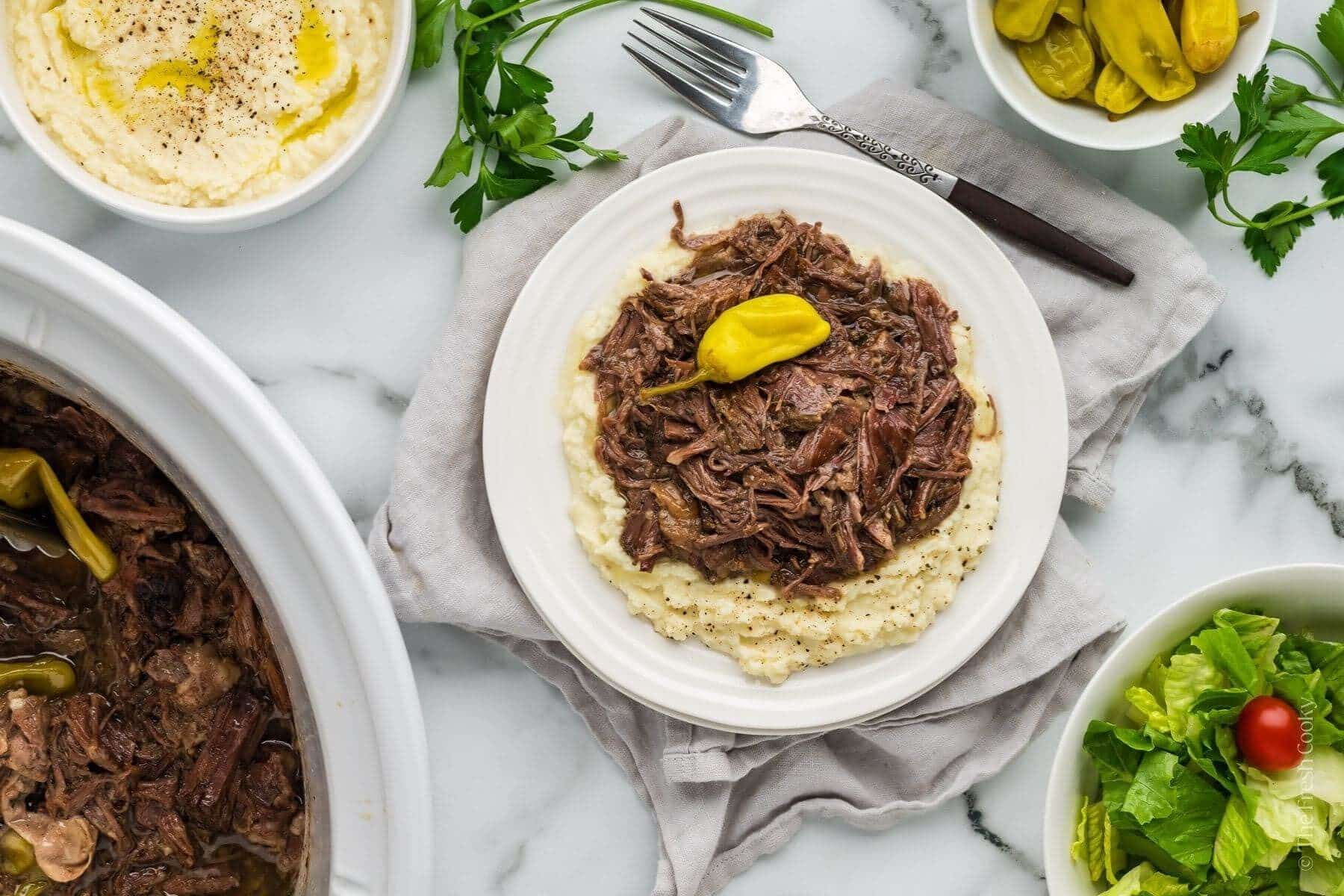 Served of Mississippi pot roasted with mashed potatoes on a plate with peppers and sald around it.