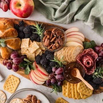 Pumpkin shaped baked brie on board with various nuts, crackers, salami, grapes and berries.