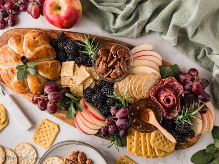 View of the full board of pumpkin brie baked in puff pastry with grapes, apples, nuts, jam, crackers, salami and blackberries.