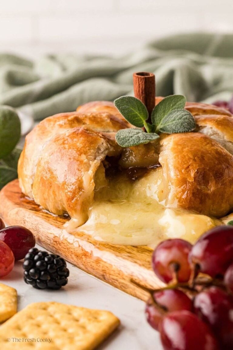 Gooey pumpkin baked brie en croute with melting cheese spilling out of the opening on a cutting board with berries and grapes.