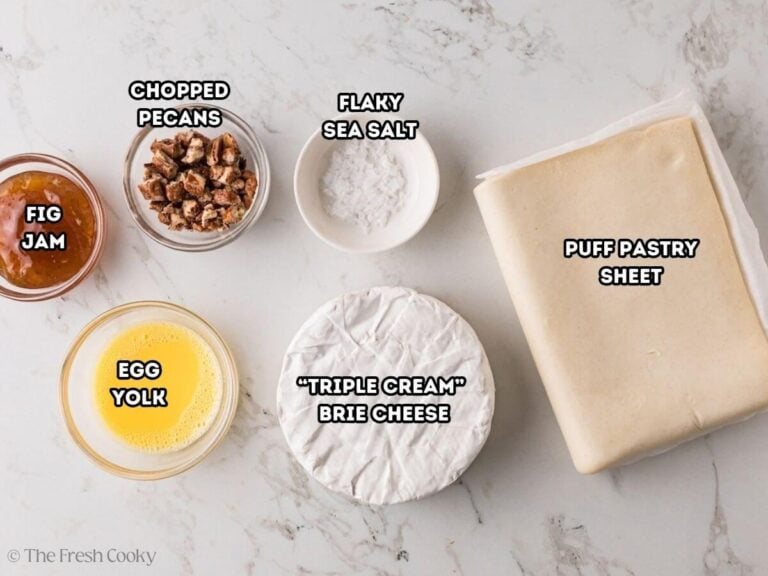 Labeled ingredients for pumpkin baked brie in puff pastry. L-R Fig jam, chopped pecans, flaky seas salt, puff pastry sheet, triple cream brie and egg yolk wash.
