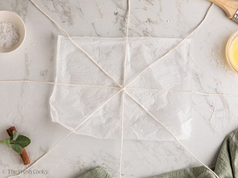 Four pieces of kitchen twine laid out like spokes on parchment.