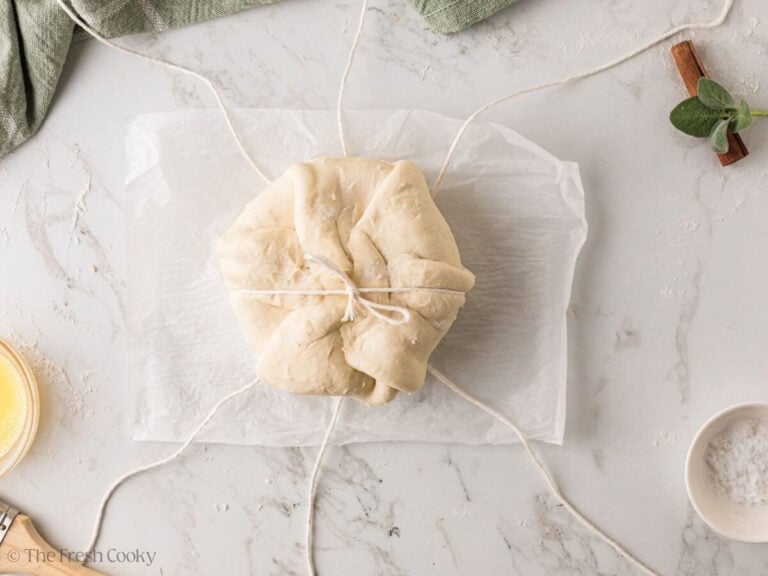 Wrapped brie set seam side up on crossed kitchen twine, with one piece tied across.