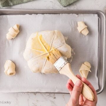 Pastry brush brushing egg wash on the pumpkin shaped puff pastry.