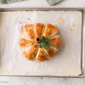Puff pastry pumpkin on baking sheet, topped with cinnamon stick and sage leaves.