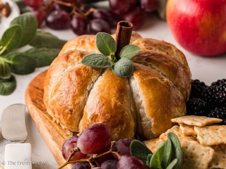 Pumpkin baked brie with a pepper stem and sage leaves on a board.