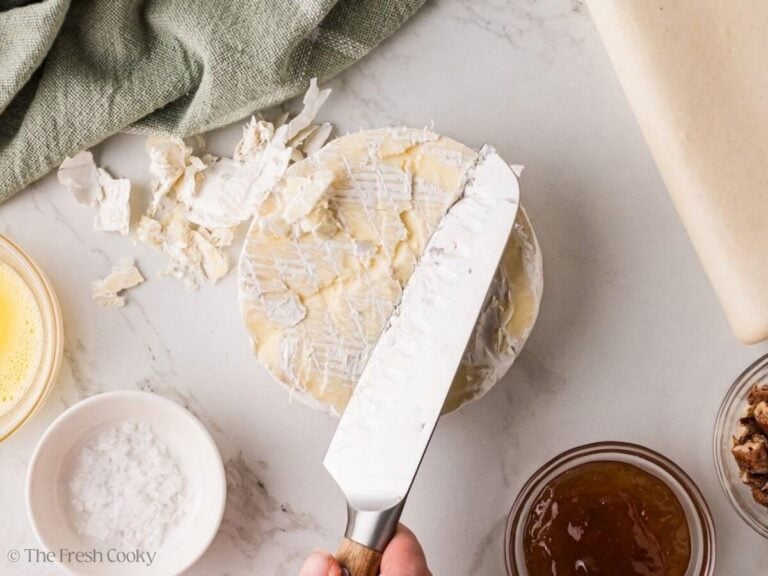 Knife trimming off the rind of a wheel of brie cheese.