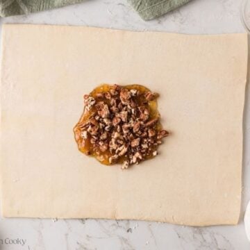 A small circle of fig jam and chopped pecans on sheet of puff pastry.