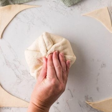 Hand wrapping and pinching together the puff pastry dough around the brie round.