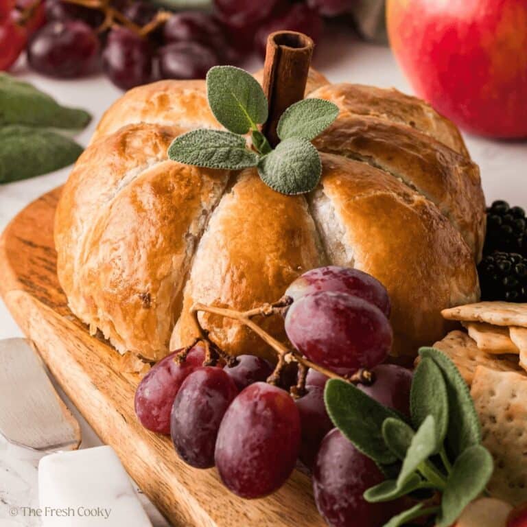 Pumpkin baked brie on a beautiful olive wood board with grapes, crackers and other fruit.