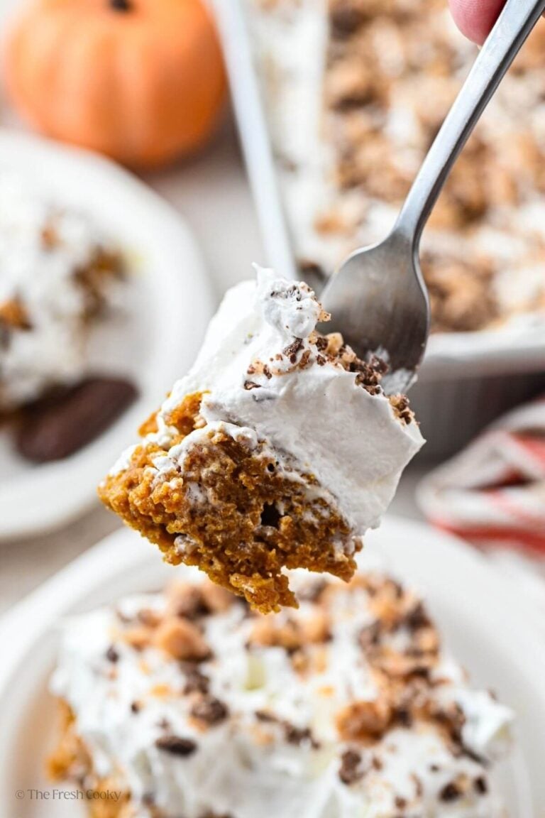 Fork with a bite of pumpkin poke cake on it hovering over a slice of cake.