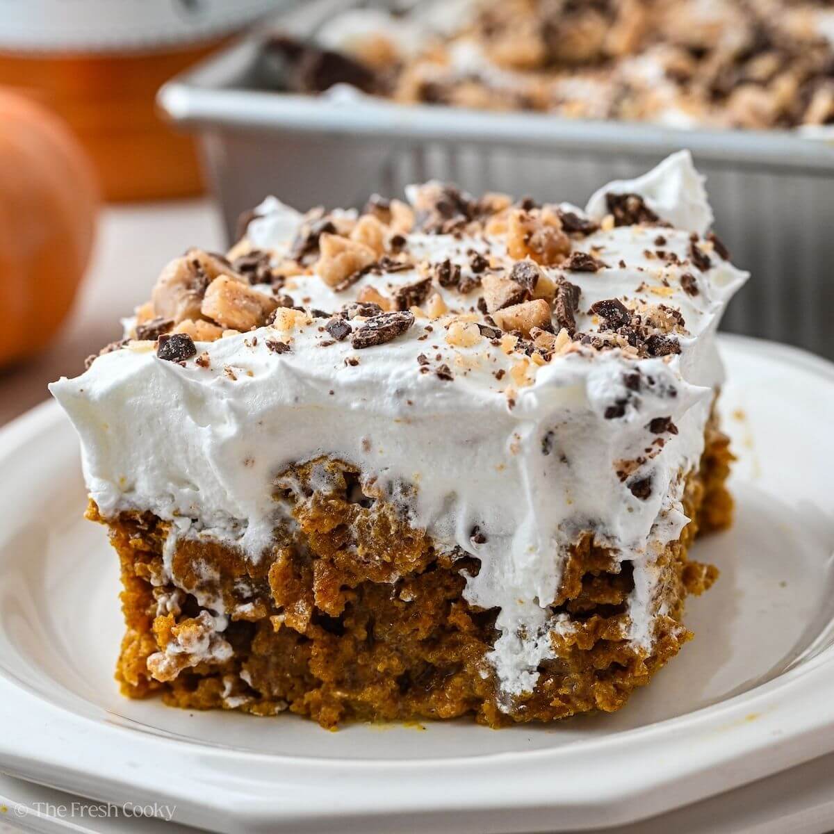 Slice of pumpkin poke cake with whipped cream and toffee on top.
