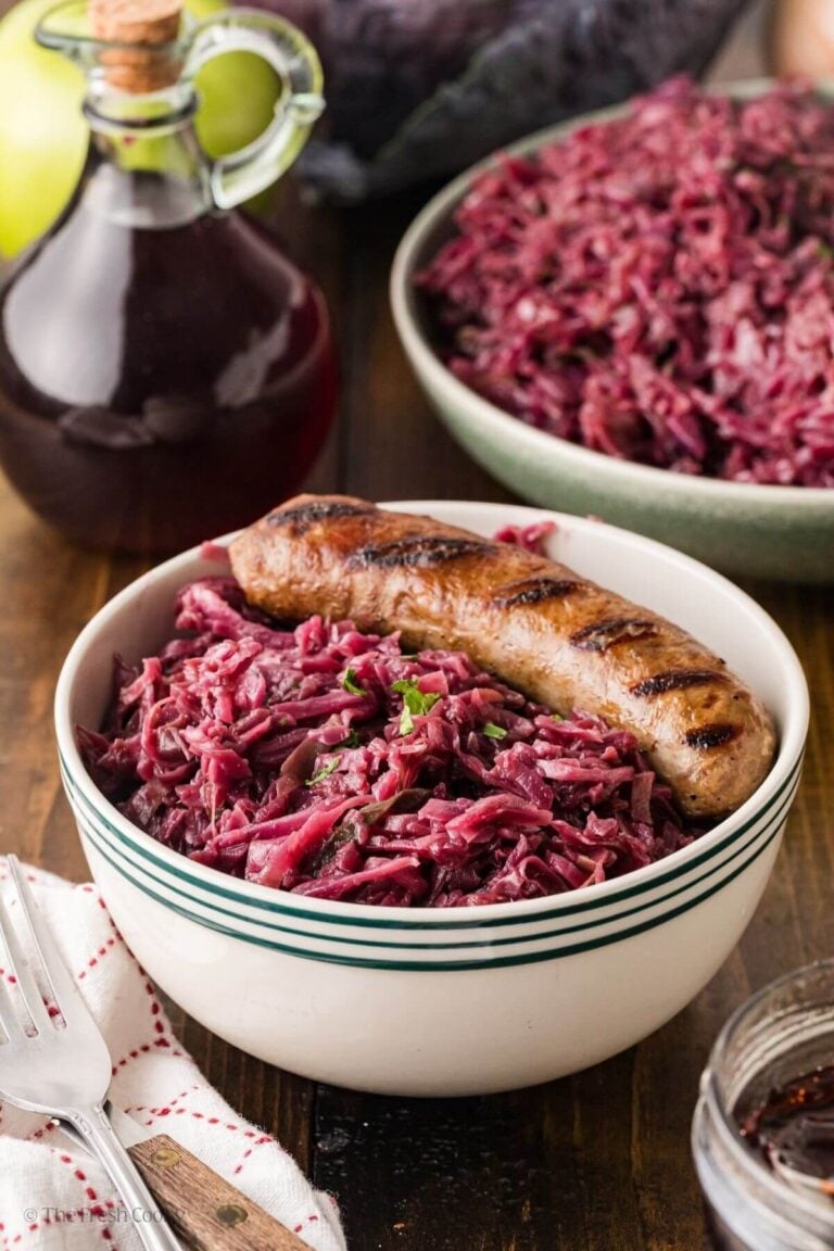 Grilled brat and rotkohl in a bowl with more rotkohl in a bowl in the background.