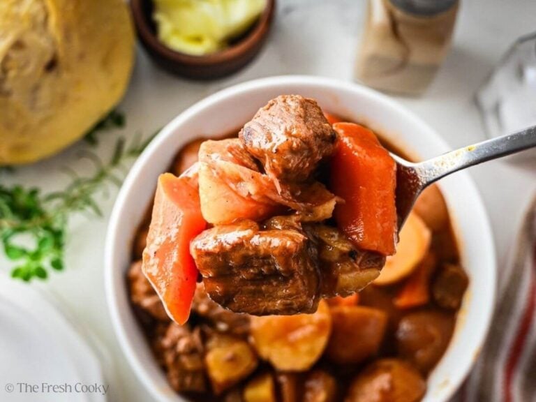 Spoonful of slow cooker beef stew hovering over a bowl of stew below it.