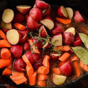 Carrots, potatoes, and herbs placed in the slow cooker.