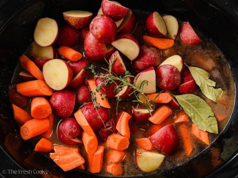 Carrots, potatoes, and herbs placed in the slow cooker.