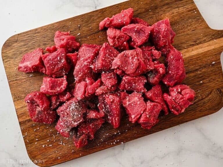Salted and peppered raw beef cubes on a cutting board.