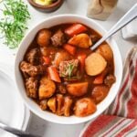 Finished beef stew served in a white bowl with a spoon.