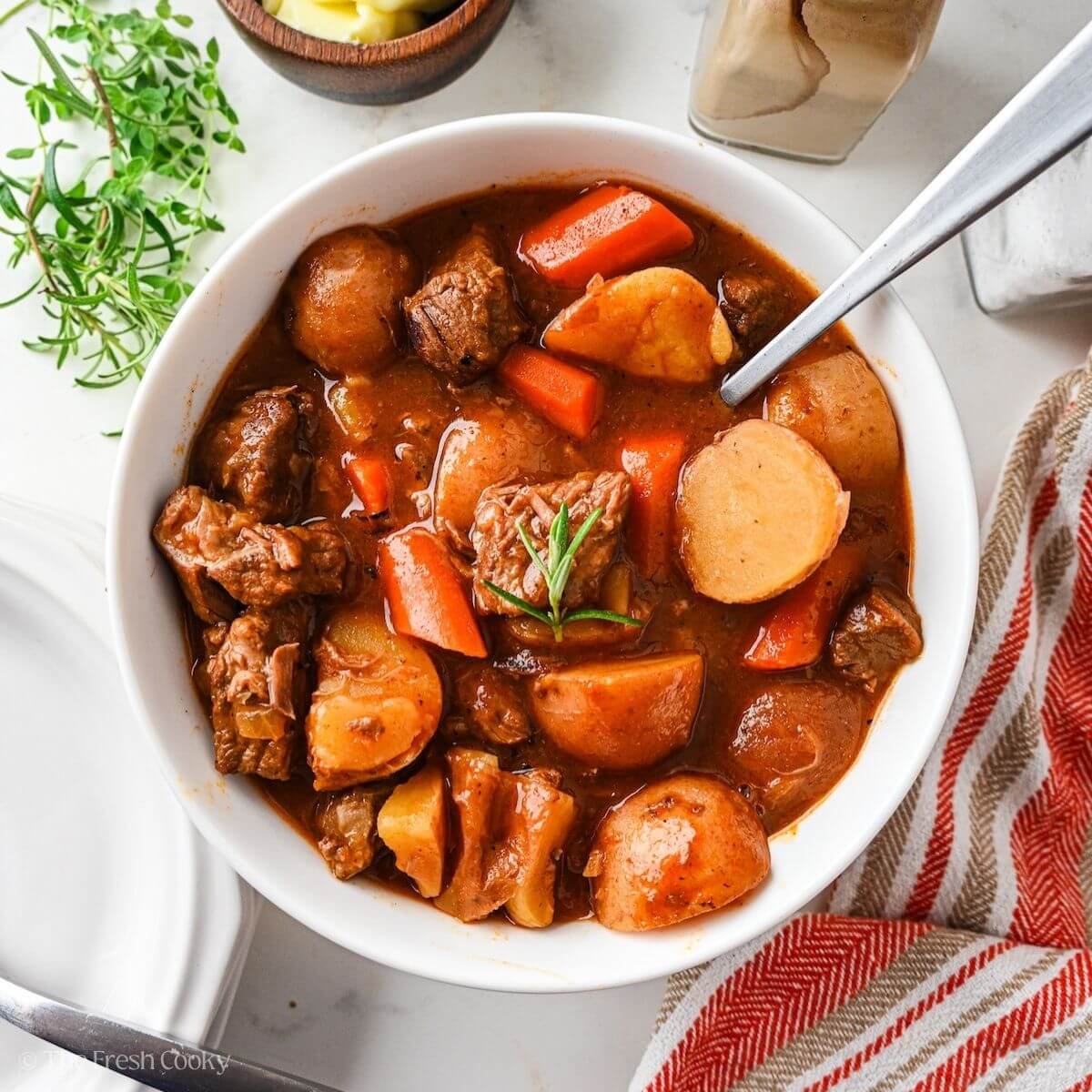 Finished beef stew served in a white bowl with a spoon.