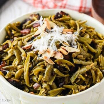 Green beans with bacon, topped with toasted almonds and parmesan cheese in a pretty white serving bowl.