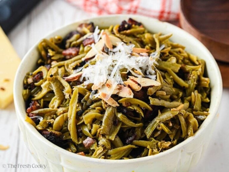 Green beans with bacon, topped with toasted almonds and parmesan cheese in a pretty white serving bowl.
