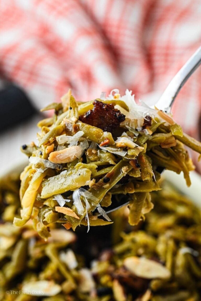 A spoonful of Southern green beans with the b owl below. Filled with crisp bacon, toasted almonds, parmesan cheese and crispy onions.