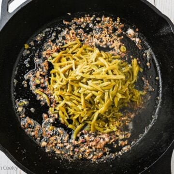 Adding drained green beans to the pan of bacon.