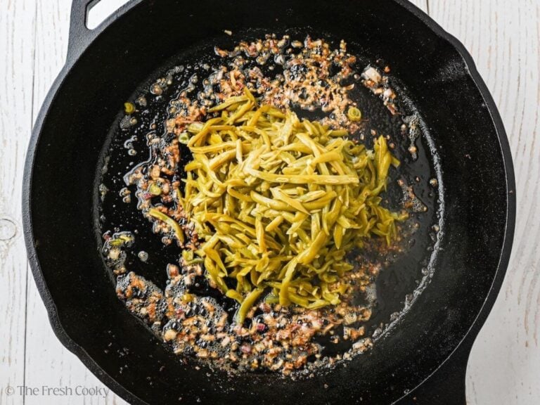 Adding drained green beans to the pan of bacon.