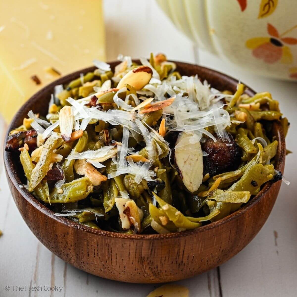 A pretty wooden bowl filled with Southern green beans with crispy bacon, toasted almonds and parmesan cheese.