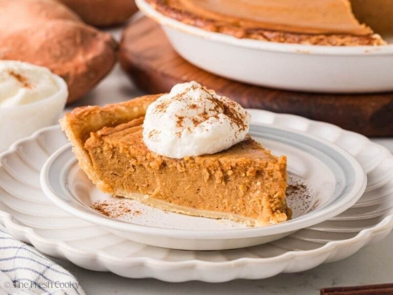 Side view of a slice of sweet potato pie on a plate with whipped cream on top.