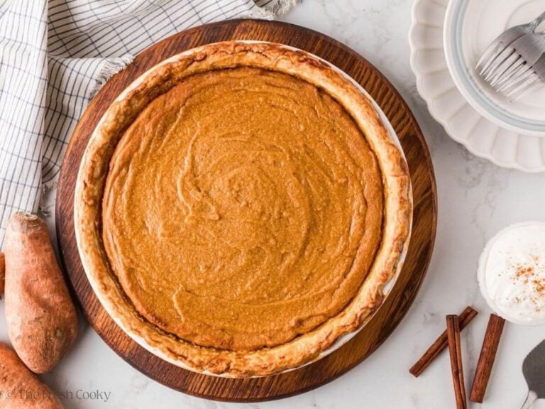 Overhead shot of a sweet potato pie in a white baking dish on a round wooden board.