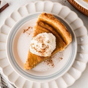 Overhead shot of a slice of sweet potato pie on a plate with whipped cream on top.