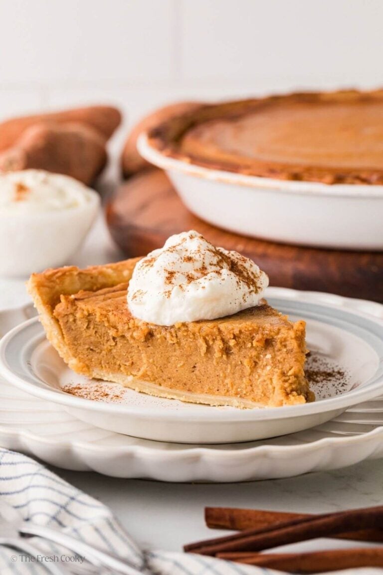 Slice of sweet potato pie on a plate with the rest of the pie in the background.