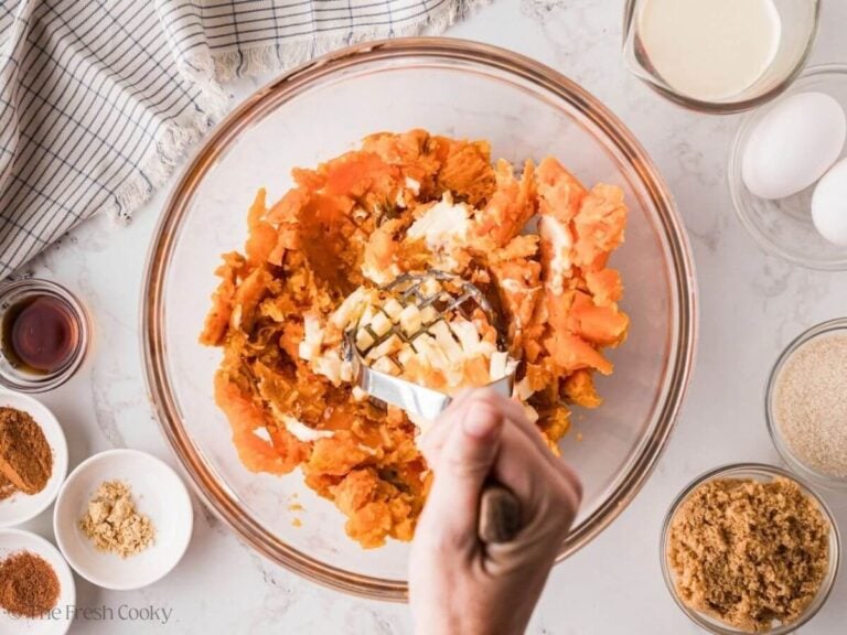 Mashing the roasted sweet potatoes and butter in a bowl.