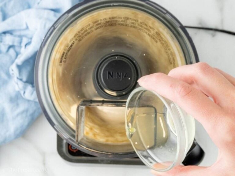 Adding almond extract to the almond paste in a food processor.
