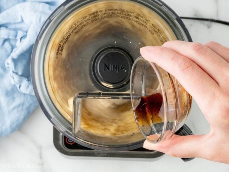 Adding vanilla extract to almond paste in a food processor.