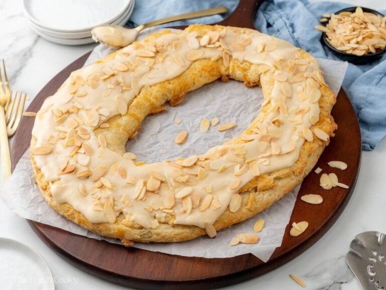 Wring shaped kringle on a round board, kringle is drizzled with a vanilla glaze and sliced almonds.