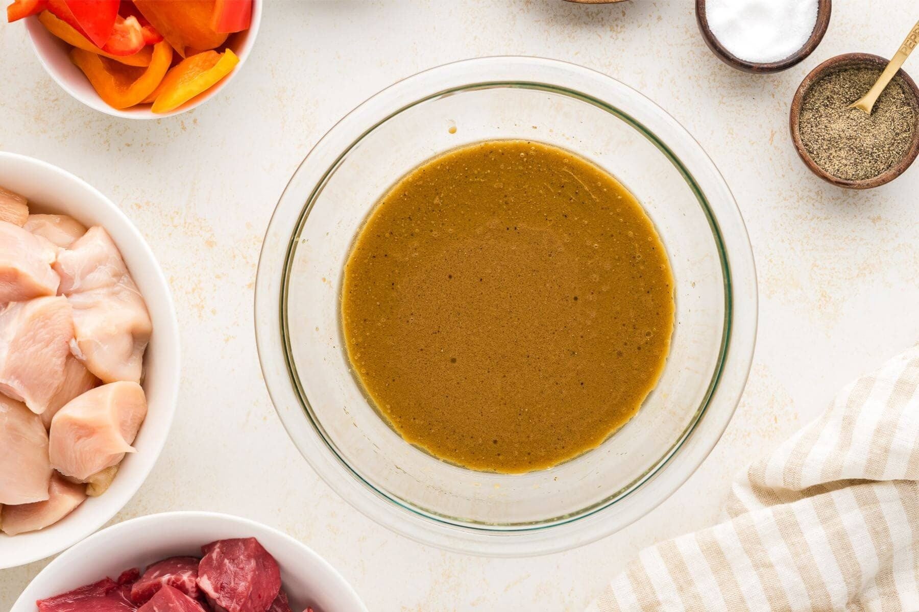 A bowl of the marinade mixture for the shish kababs surrounded by the uncooked kabab meat and vegetables.