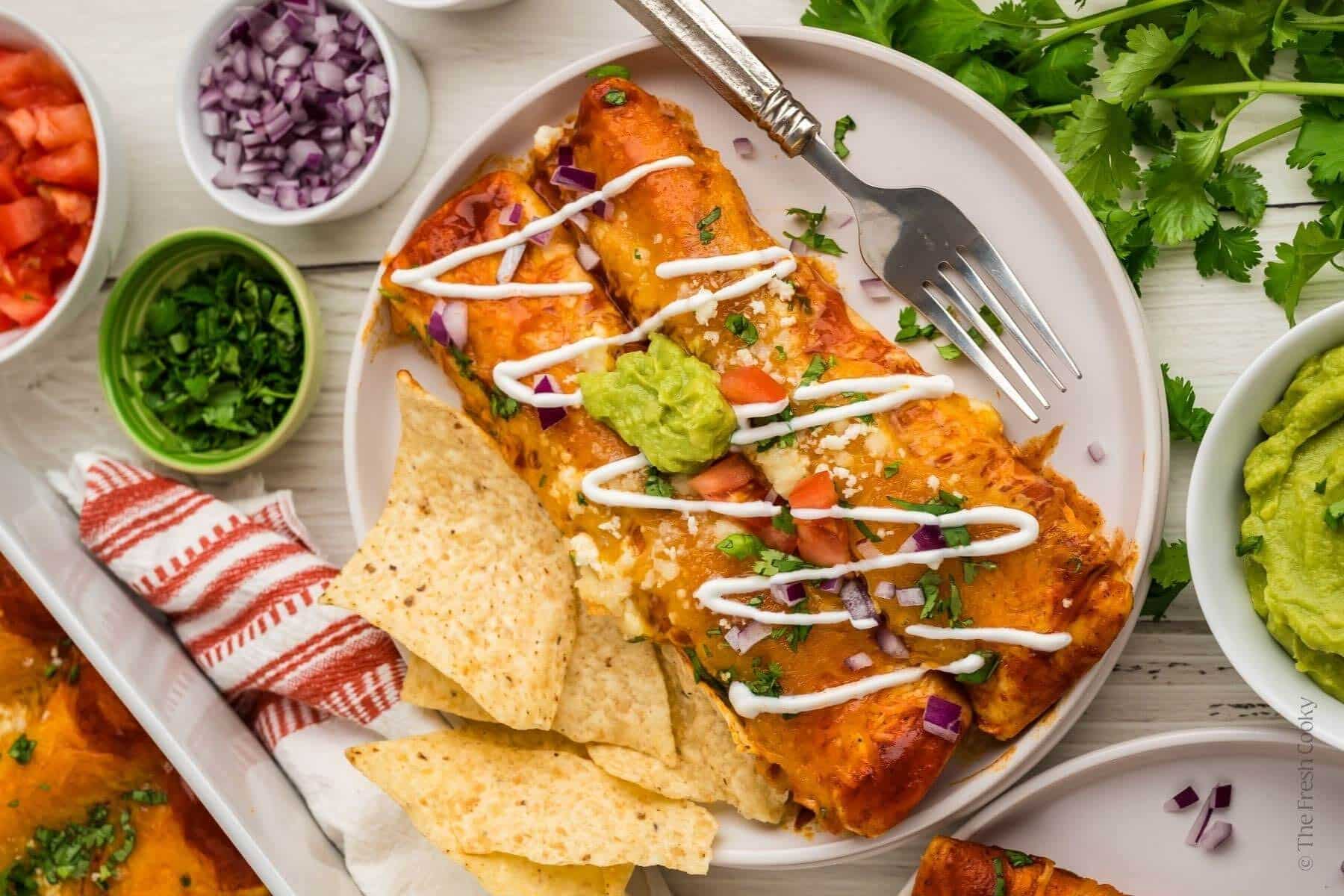Overhead shot of chicken enchiladas with a side of chips and other toppings on the side.