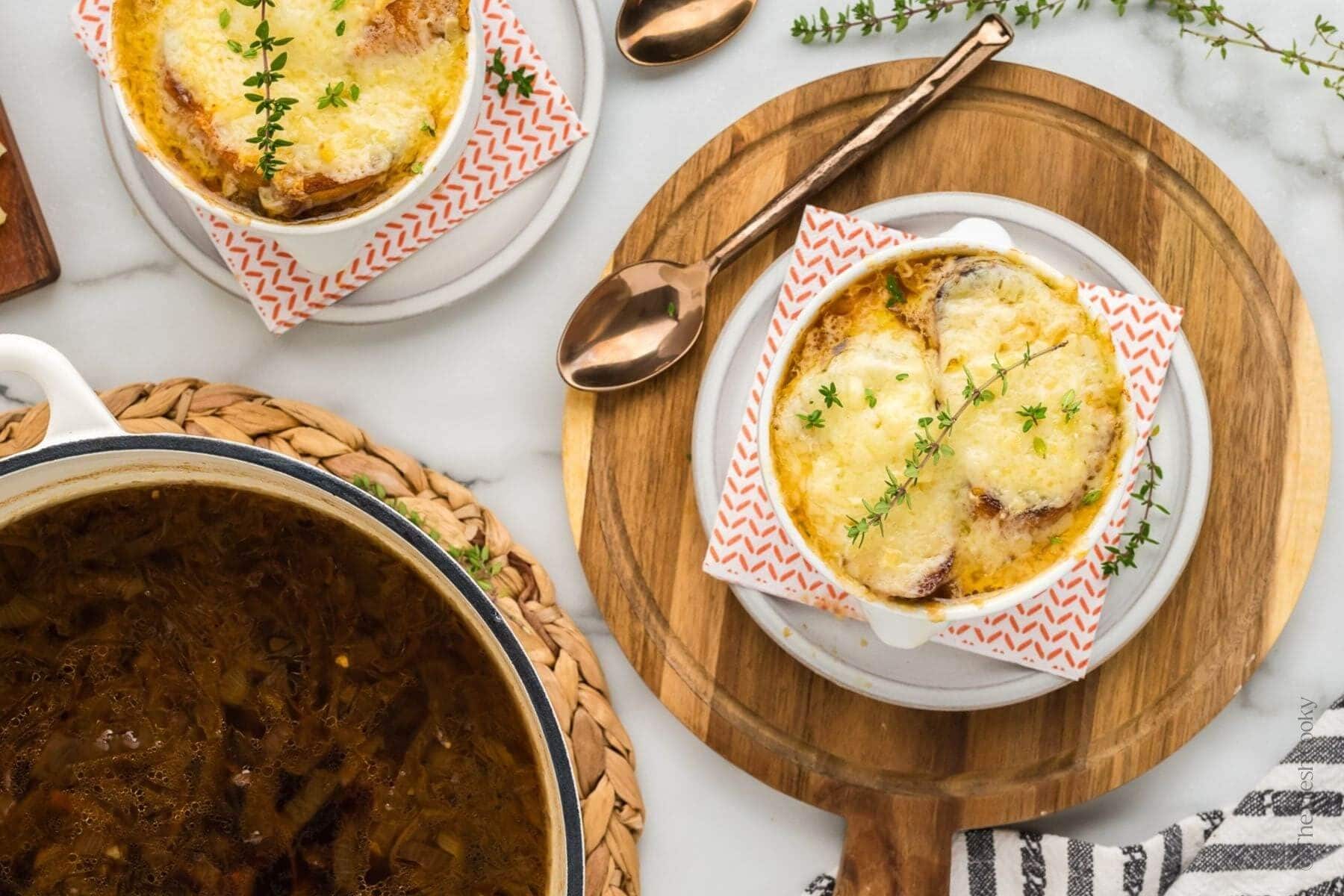 Overhead shot of two bowls of French onion soup and a pot of it in the corner.