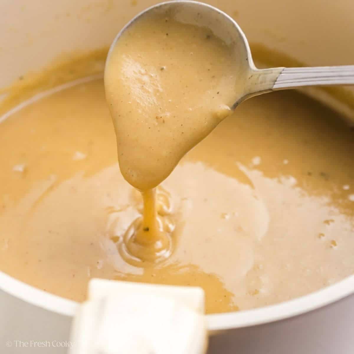 Spoon scooping up some turkey giblet gravy from a saucepan.