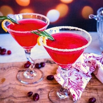 Two martini glasses full of bright red cranberry lemon drop martini, garnished with rosemary and lemon peel.