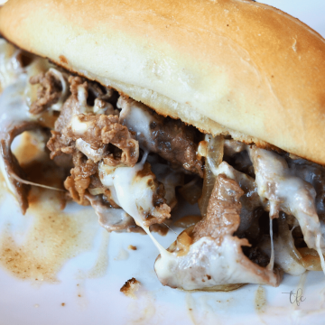 Philly cheese steak sandwich on a tray with french fries surrounding it.