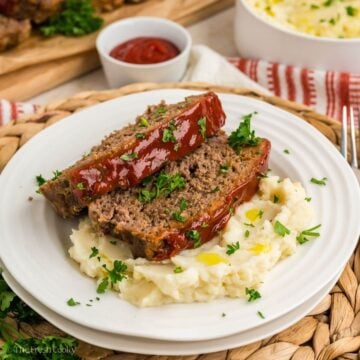 White plate with mashed potatoes and two slices of meatloaf on top.